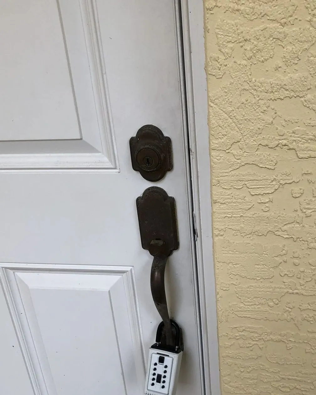 Before: worn dark bronze deadbolt and handleset with a lockbox hanging from the handle