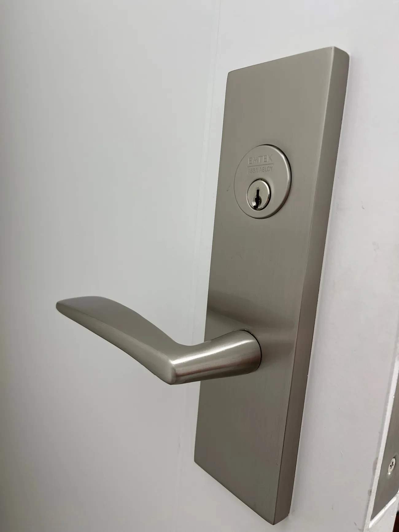 Emtek satin nickel mortise entry set with a lever on a white door