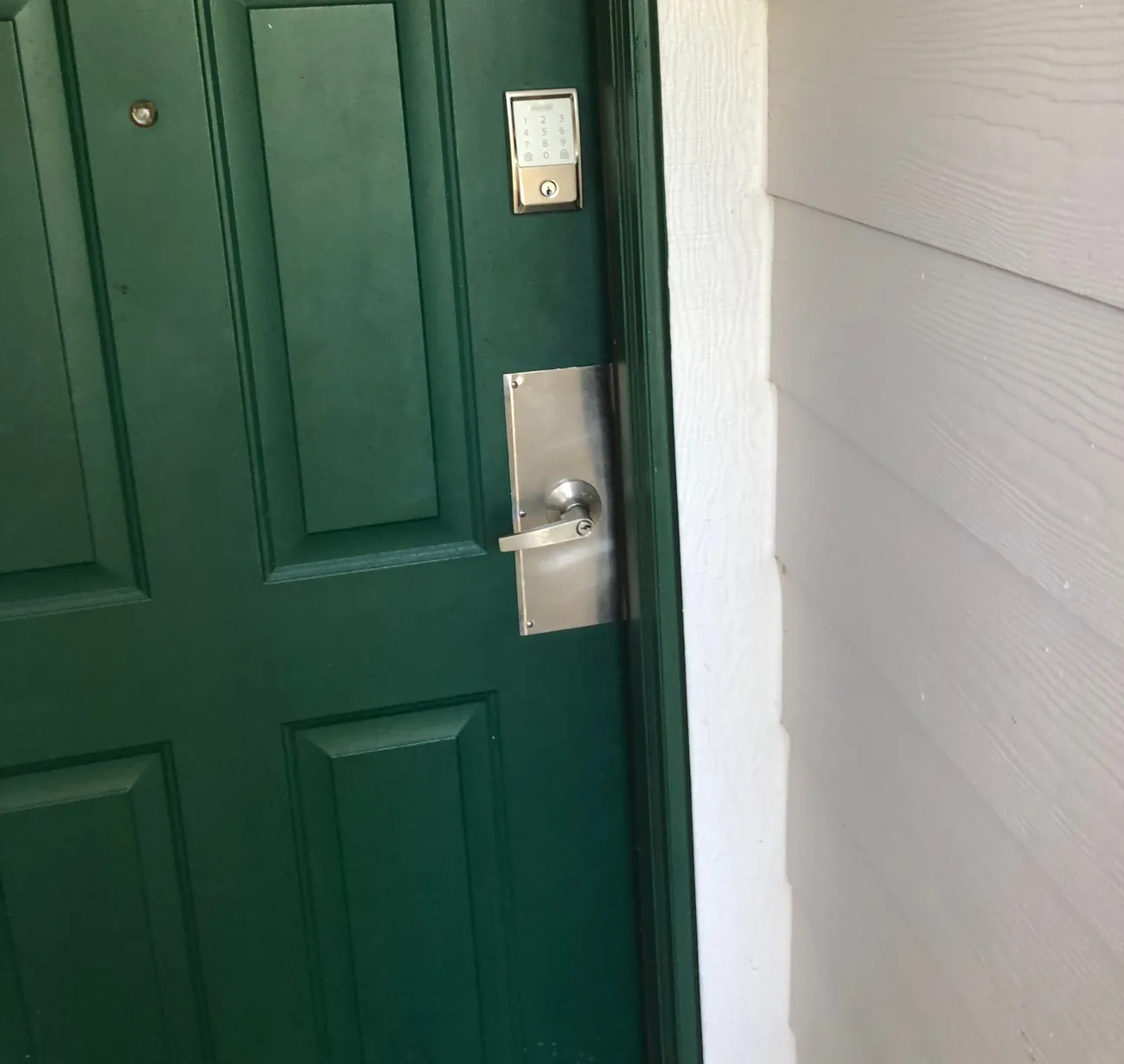 Green entry door with a keypad lock and a lever on a stainless plate