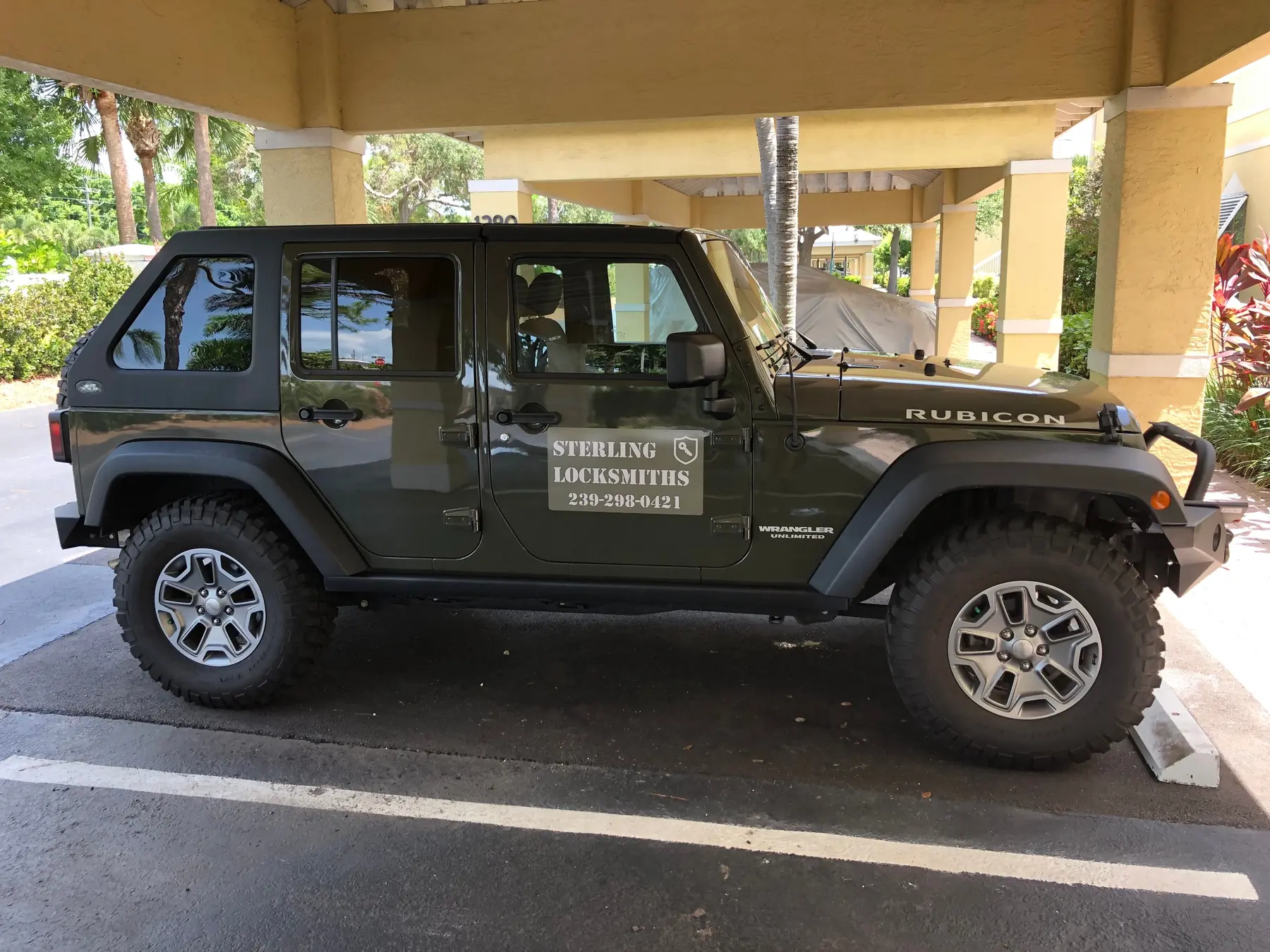 The Sterling Locksmiths olive drab Jeep Wrangler Rubicon, with the company name and phone number on the door, parked under a carport in Naples, Florida